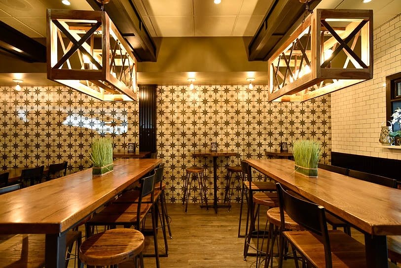 The dining room, with wooden tables, patterned tile walls and lantern pendant lights