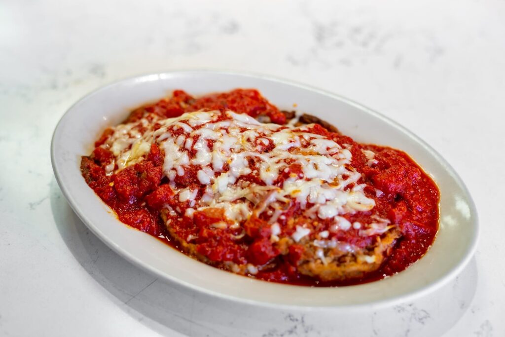 Eggplant parmigiana under chunky tomato sauce and melted mozzarella in a white oval dish