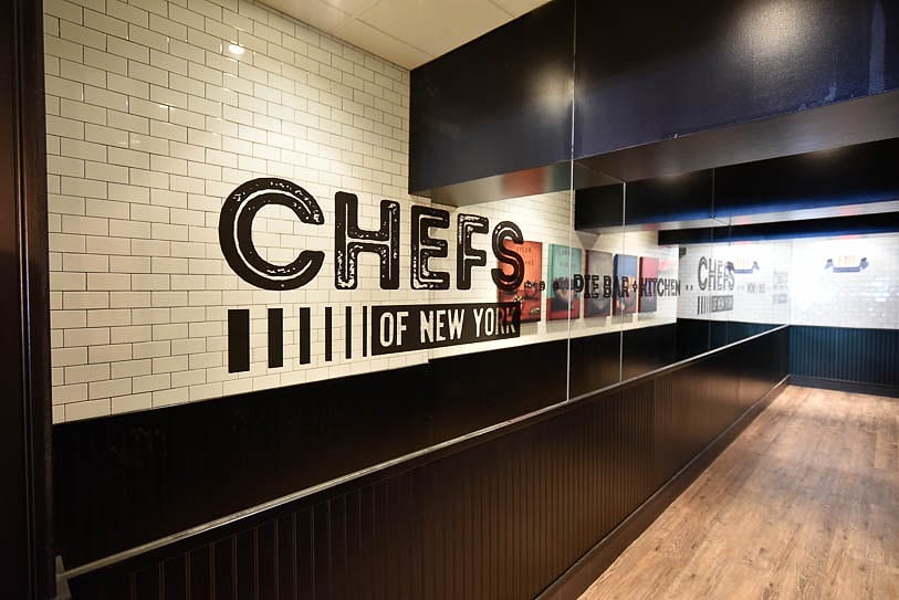 The Chefs of New York logo painted on the white subway-tile wall inside the restaurant