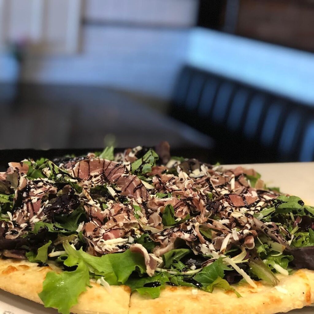 Prosciutto pizzetta topped with baby greens, prosciutto, shaved pecorino romano and a balsamic glaze