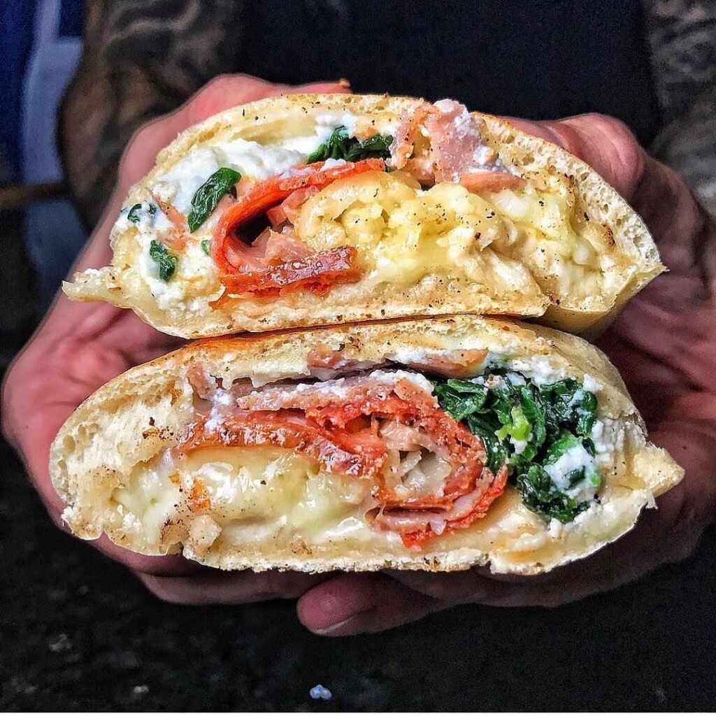 A stuffed dough roll cut in half to show layers of cured meats, ricotta, spinach and melted cheese