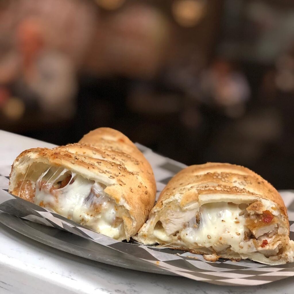 A sesame-topped stuffed roll cut open, filled with chicken and stretchy melted mozzarella