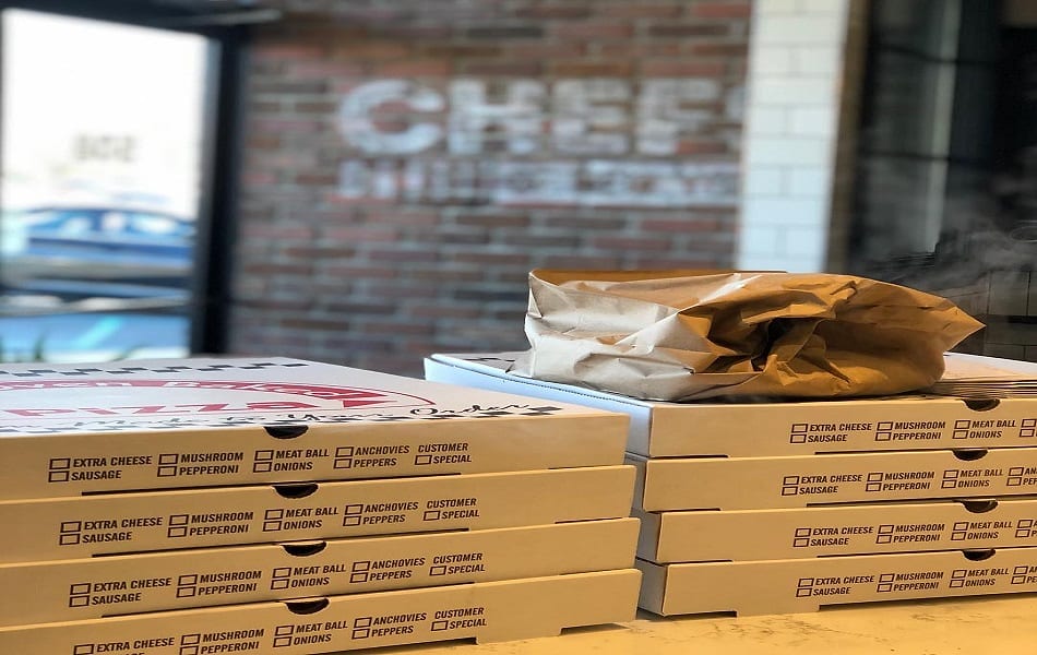 Stacked pizza boxes ready for pickup in front of the painted Chefs logo on the brick wall