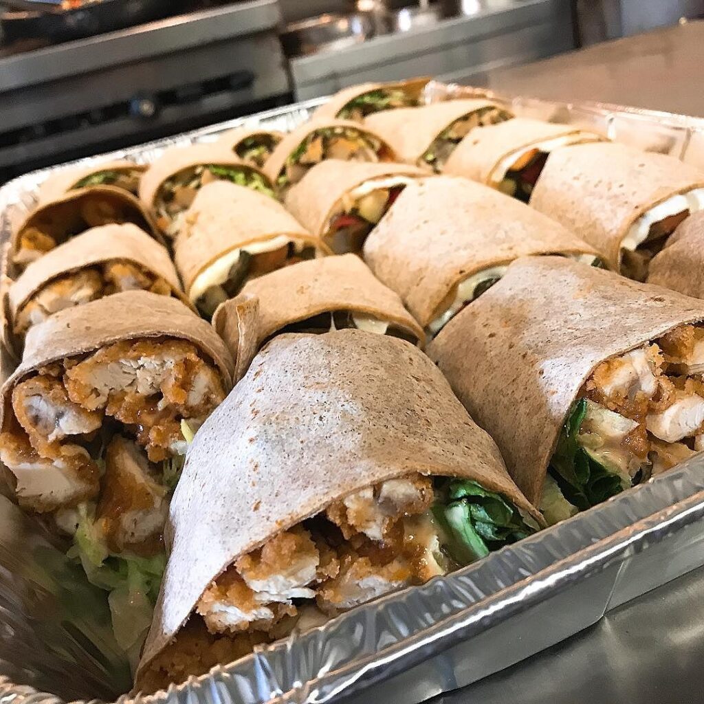 A catering tray of halved wraps filled with crispy chicken and greens